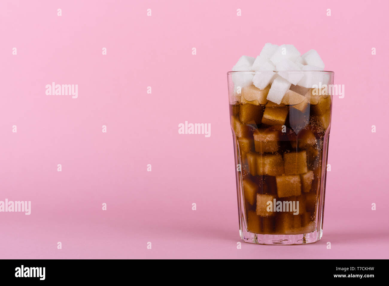 Trinken Glas von Klumpen Zucker Würfel und weich Cola trinken auf Rosa pastell Hintergrund. Unhealthly Ernährung mit süßen zuckerhaltigen Softdrinks Konzept. Stockfoto