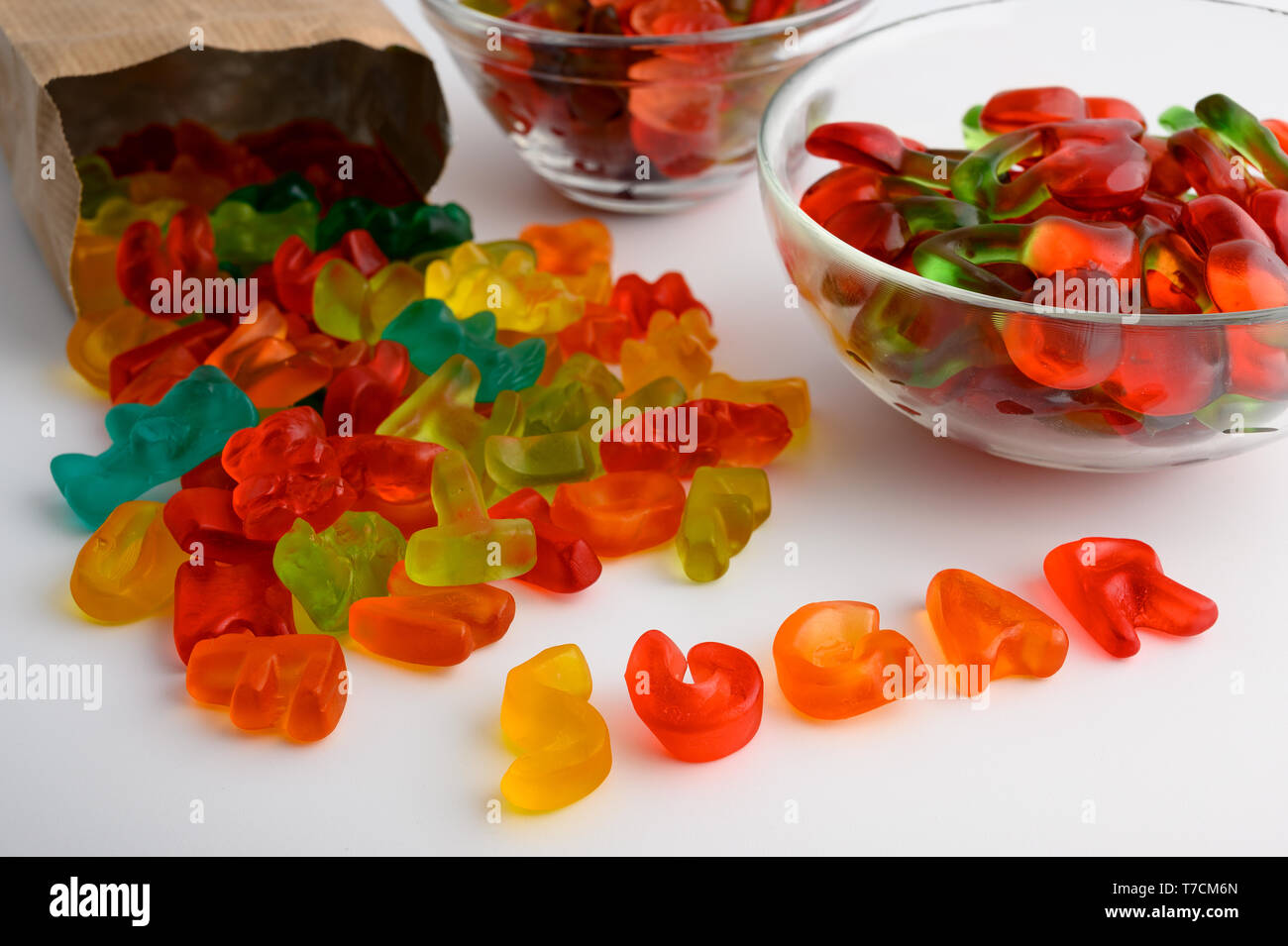 Glasschalen und Paper bag von bunten Gummibärchen Bonbons auf weißem Hintergrund. Das Wort 'Sugar', mit Süßigkeiten geschrieben Stockfoto