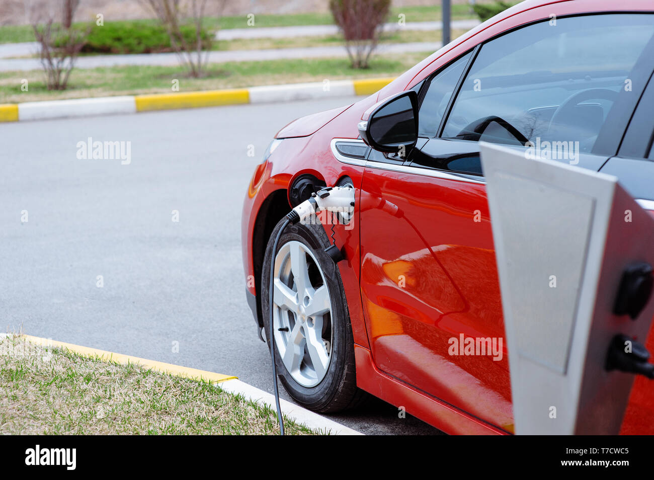 EV Auto oder elektrischen rotes Auto an der Ladestation mit Netzkabel Netzteil in unscharfer Natur mit weichen hellen Hintergrund gesteckt. Umweltfreundliche ändern Stockfoto