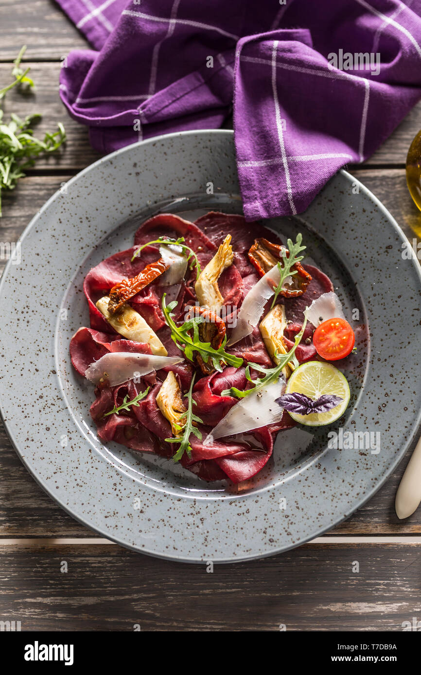 Carpaccio vom Rind auf Platte mit getrockneten Tomaten Artischocken Rucola und Parmesan Stockfoto
