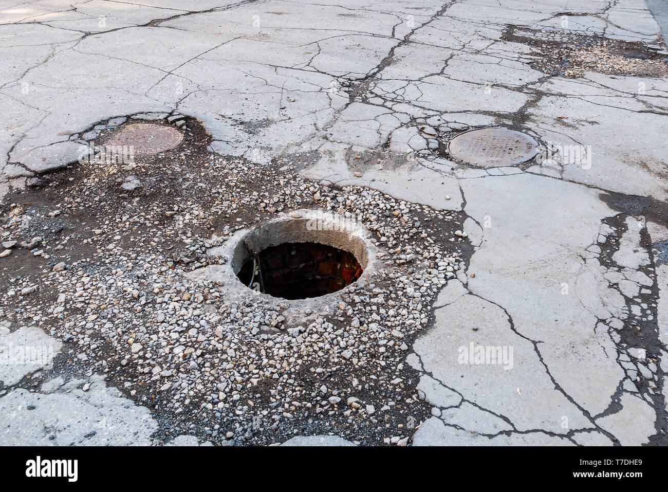 Ungesicherte Abwasserkanal Mannloch auf der Asphaltstraße öffnen. Gefährliche Grube auf der Straße. Alte Kanalisation gut Klappe auf der Straße Stockfoto