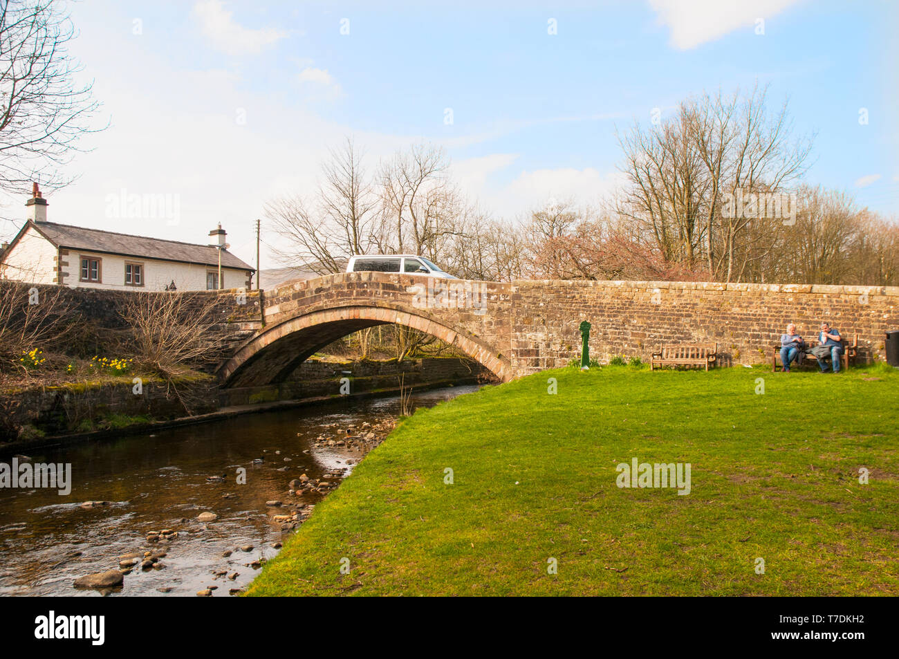 Paar auf einer Bank sitzen durch steinerne Brücke über den Fluss Dunsop auf der Straße in Dunsop Brücke Dorf Trog von Bowland Lancashire England Großbritannien Stockfoto