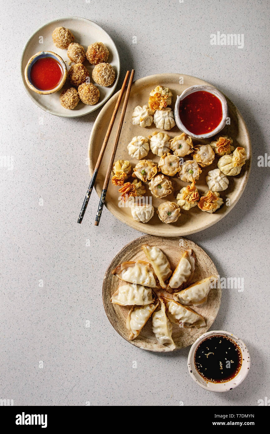 Dim Sum Gyozas asiatische gebratene Knödel Party mit verschiedenen Soßen in Keramik Teller serviert und Schüsseln mit Stäbchen über Grau gefleckten Hintergrund. Stockfoto