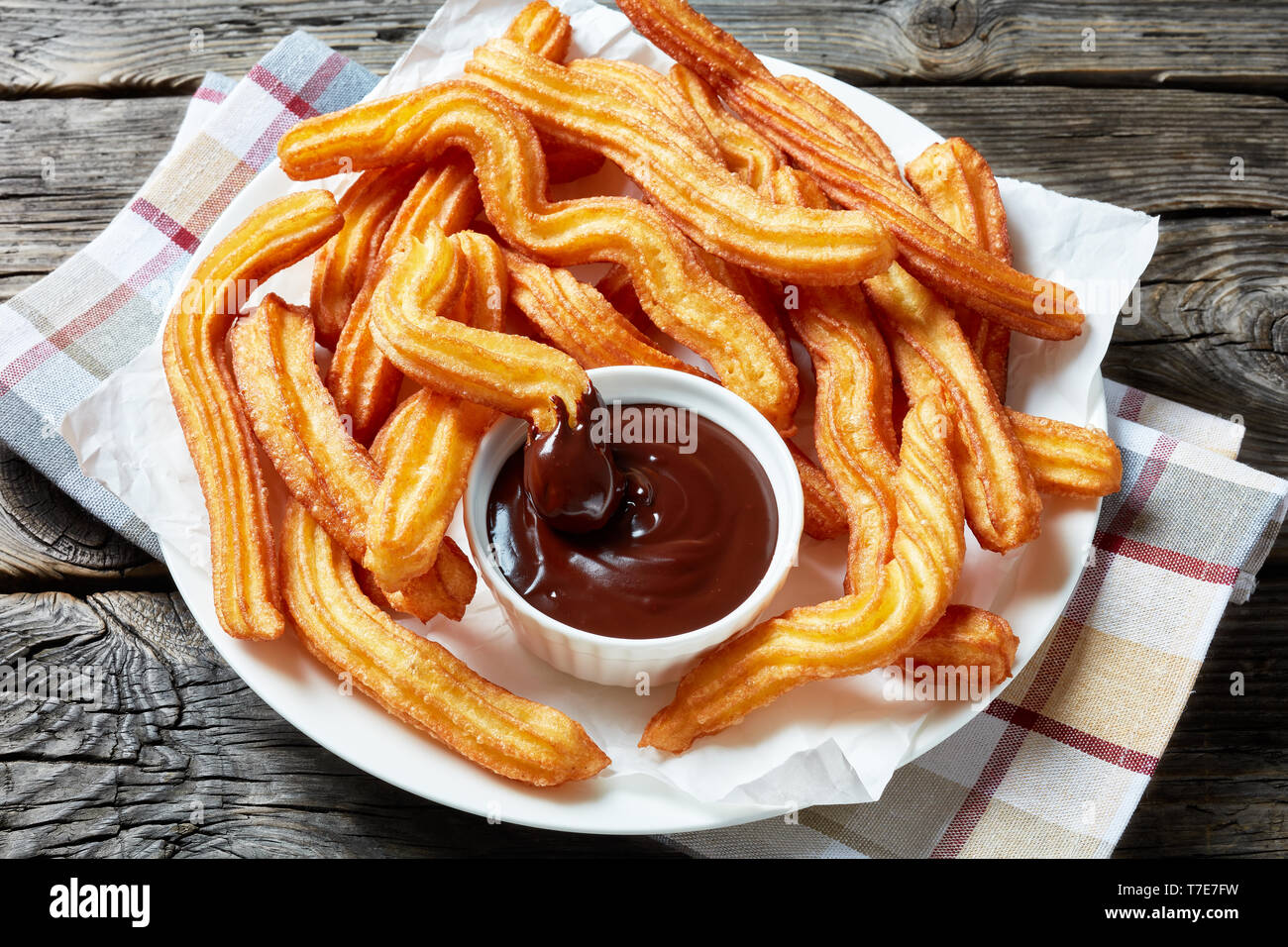 Close-up Churros - Traditionelle spanische und mexikanische Dessert auf eine weiße Platte mit Schokoladensauce auf einem Holztisch mit Serviette, horizontale Ansicht her Stockfoto