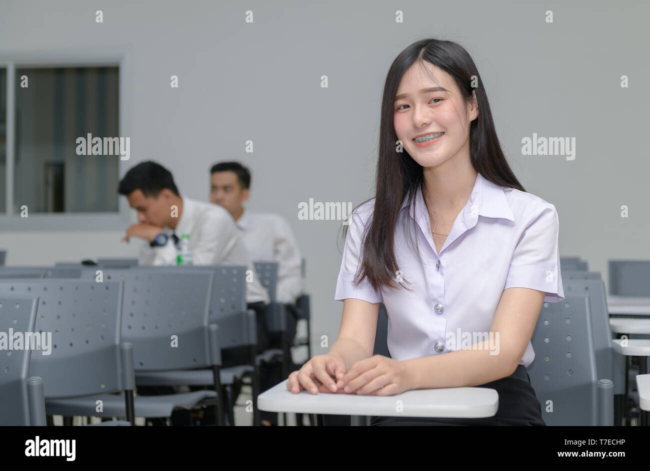 Portrait von cute Asian Girl student mit Klammern an den Zähnen, am Schreibtisch sitzen und studieren an der Universität im Klassenzimmer, Bildung Konzept Stockfoto