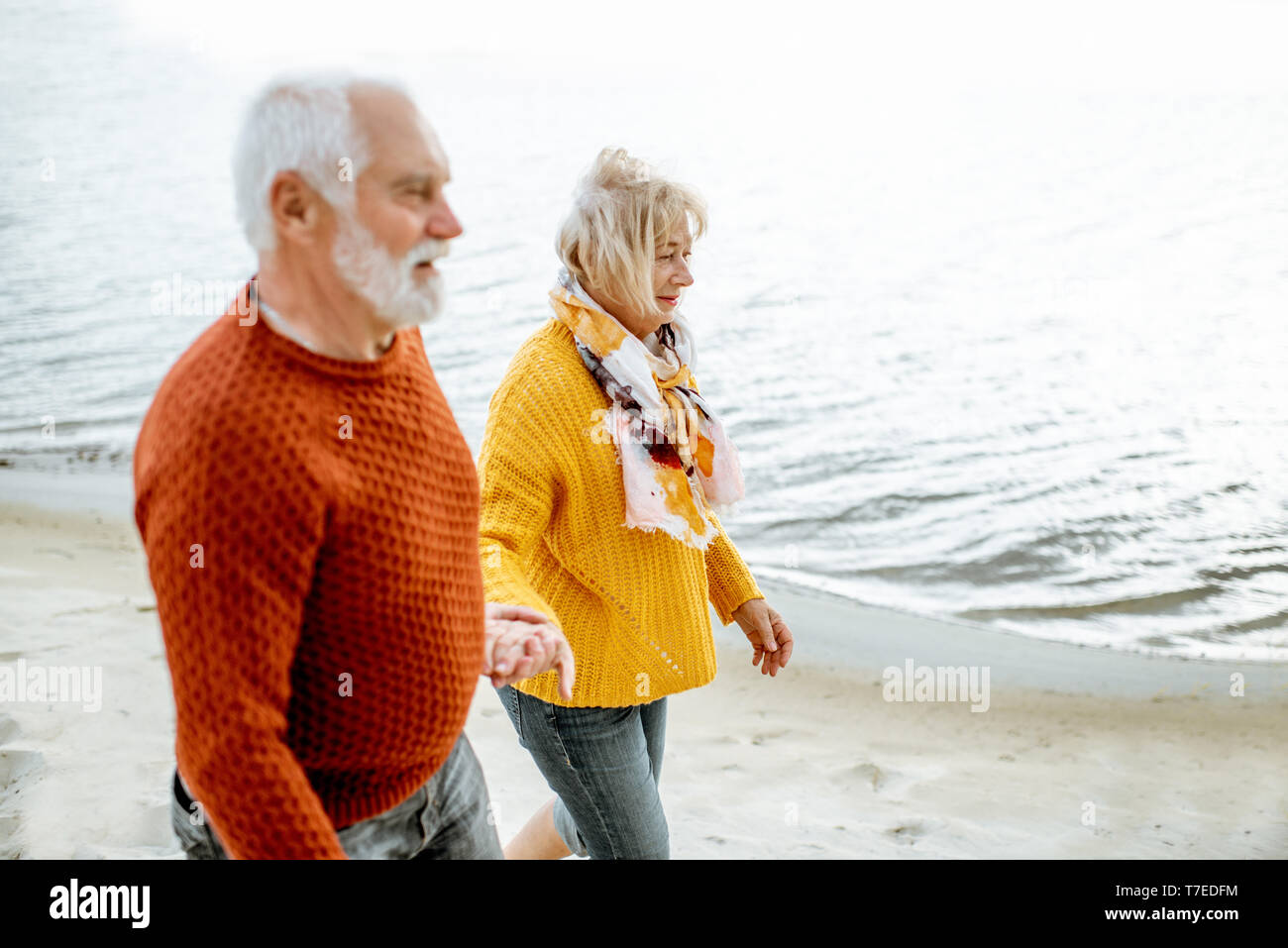 Schönes älteres Ehepaar in bunten Pullover zu Fuß am Sandstrand, genießen freie Zeit im Ruhestand in der Nähe des Meeres gekleidet Stockfoto