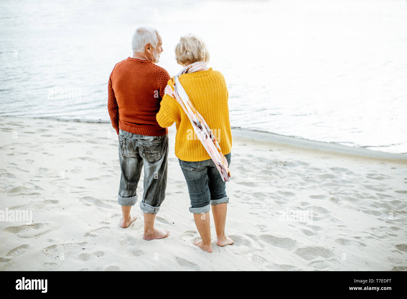 Senior Paar in bunten Pullover Natur geniessen gemeinsam auf dem Sandstrand in der Nähe des Meeres stehen, Rückansicht gekleidet Stockfoto
