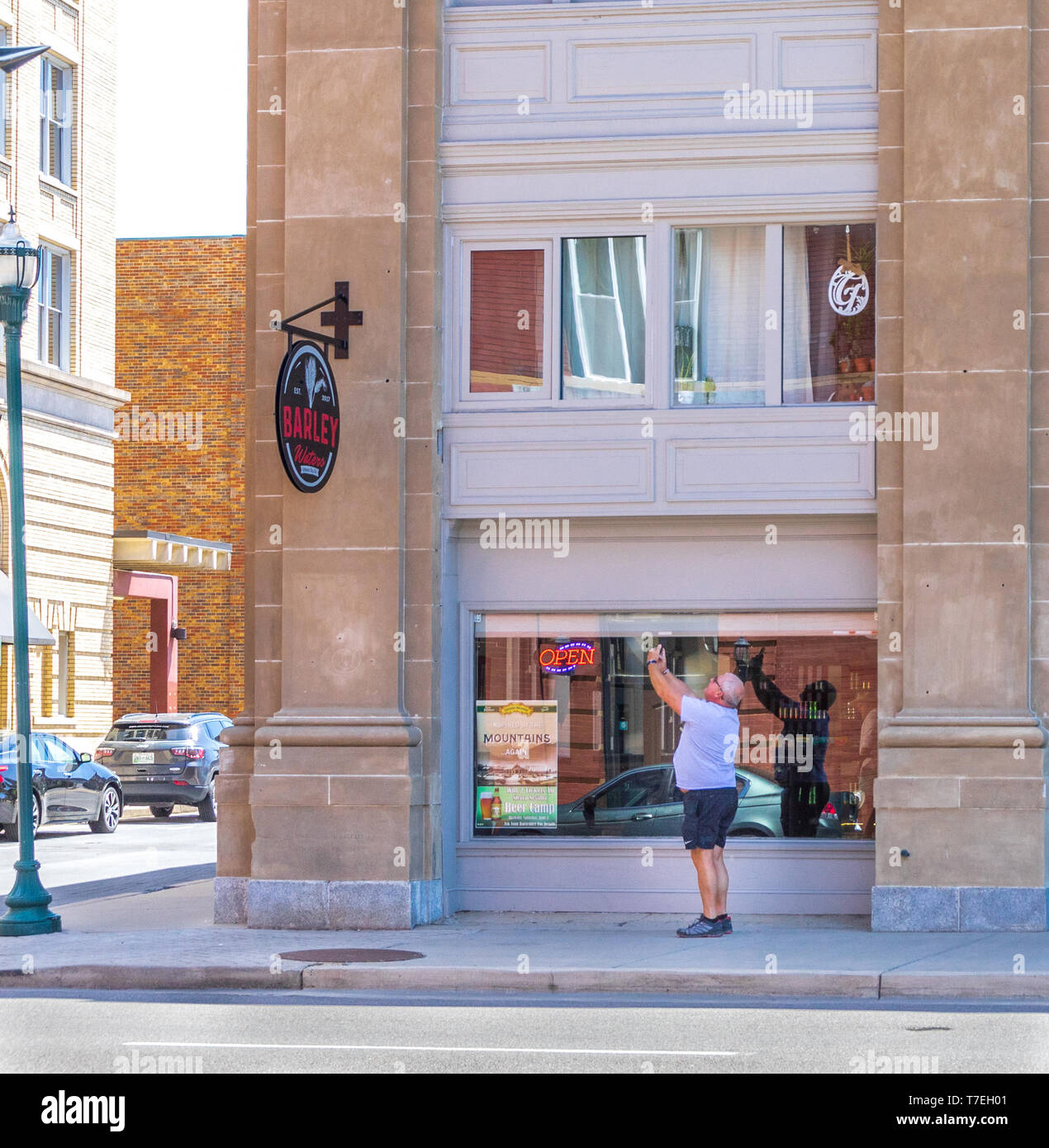 JOHNSON CITY, TN, USA -4/27/19: Ein Mann mittleren Alters nimmt ein smart phone Bild der Gerste Wasser Zeichen hängen von der alten Tennessee National Bank. Stockfoto