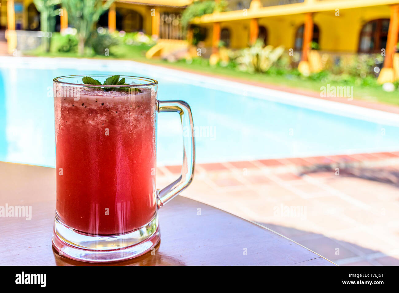 Glas kalte, erfrischende, Rot, Wassermelone Smoothie in Glas mit mint Sprig auf Tisch außerhalb von Schwimmbad an einem sonnigen Tag. Stockfoto