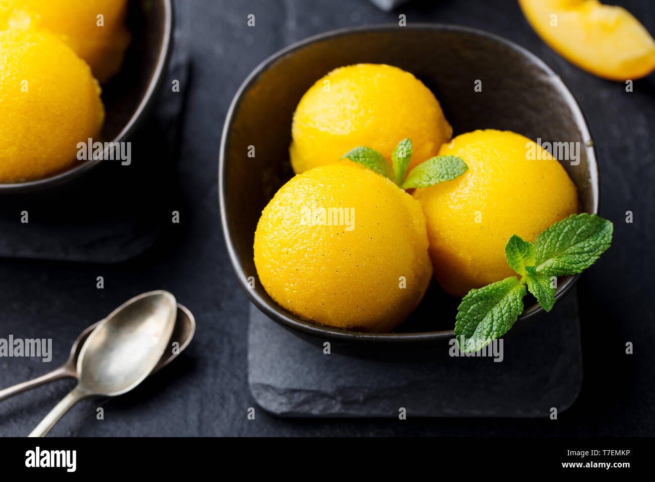 Mango und Pfirsich Eis, Tropical Fruit Sorbet in schwarz Schüssel auf schiefer Hintergrund. Close Up. Stockfoto