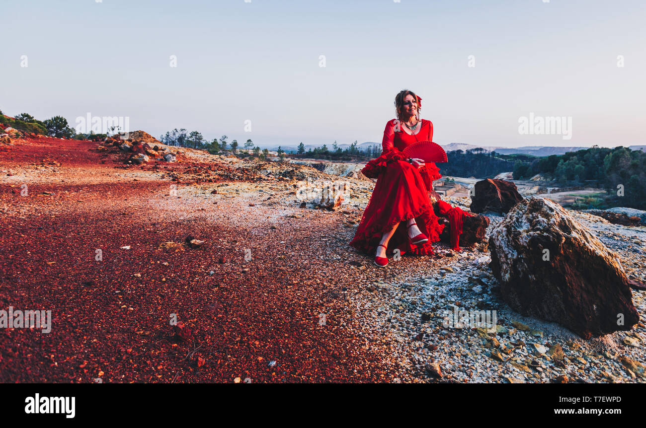 Schöne Frau in Rot flamenco Kleid auf Riotinto Minen sitzt auf einem Stein posing Stockfoto