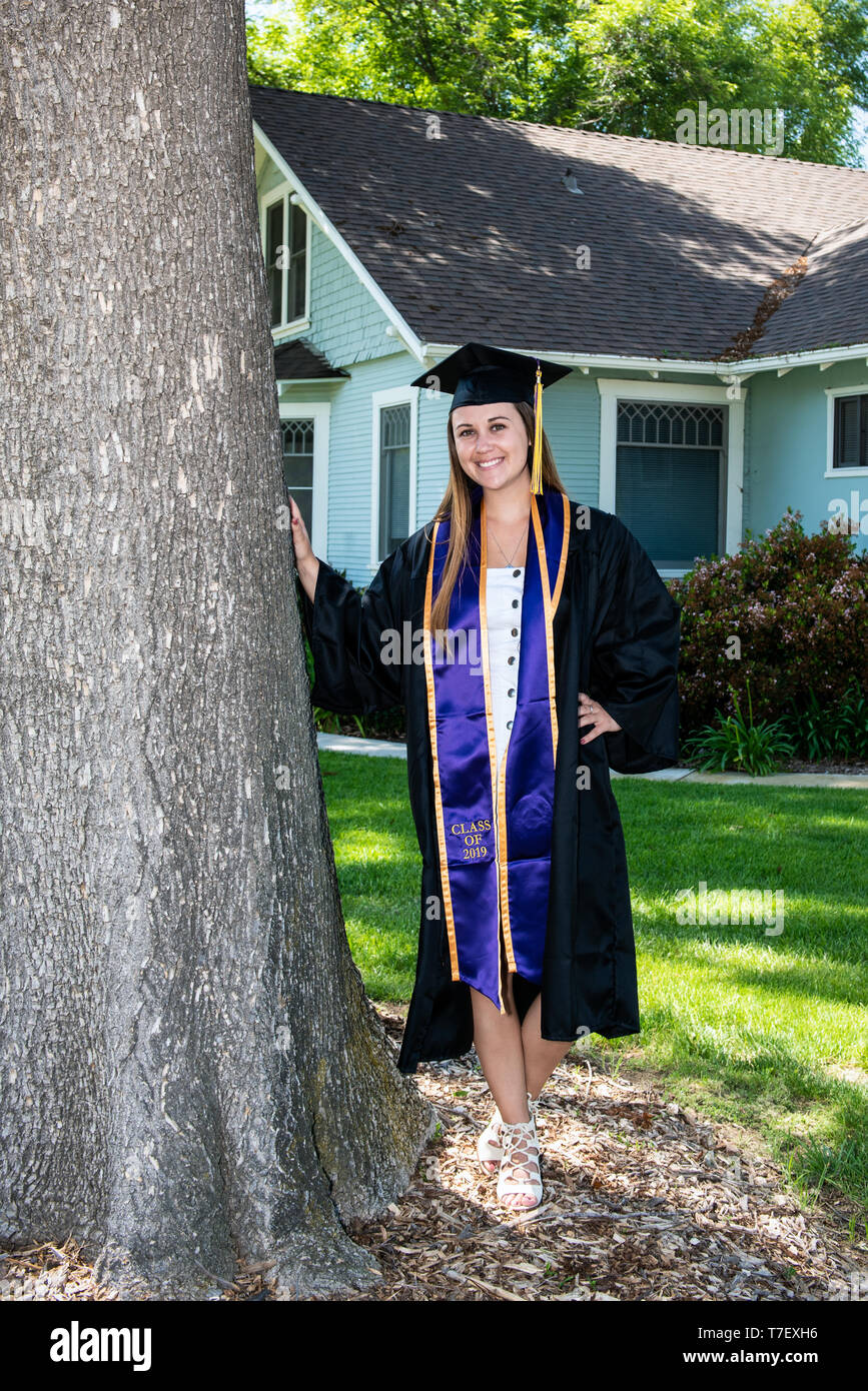 Schöne junge Schülerin lächelnd mit Vollendung während gegen Baum im Vorgarten des Hauses gelehnt. Stockfoto