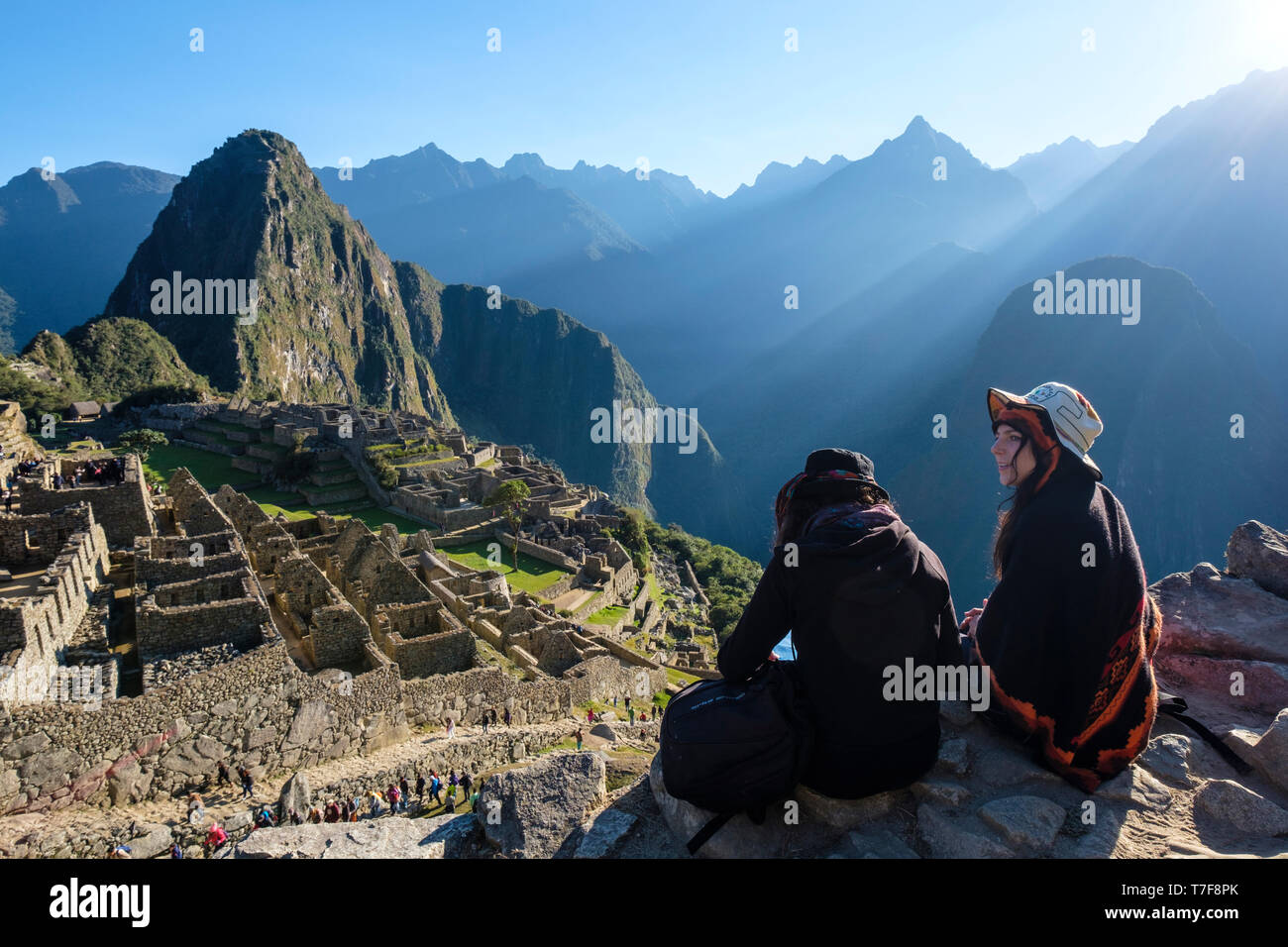 Zwei weiße Mädchen sitzen und genießen einen wunderschönen Blick auf die außergewöhnliche archäologische Stätte Machu Picchu, Peru Stockfoto