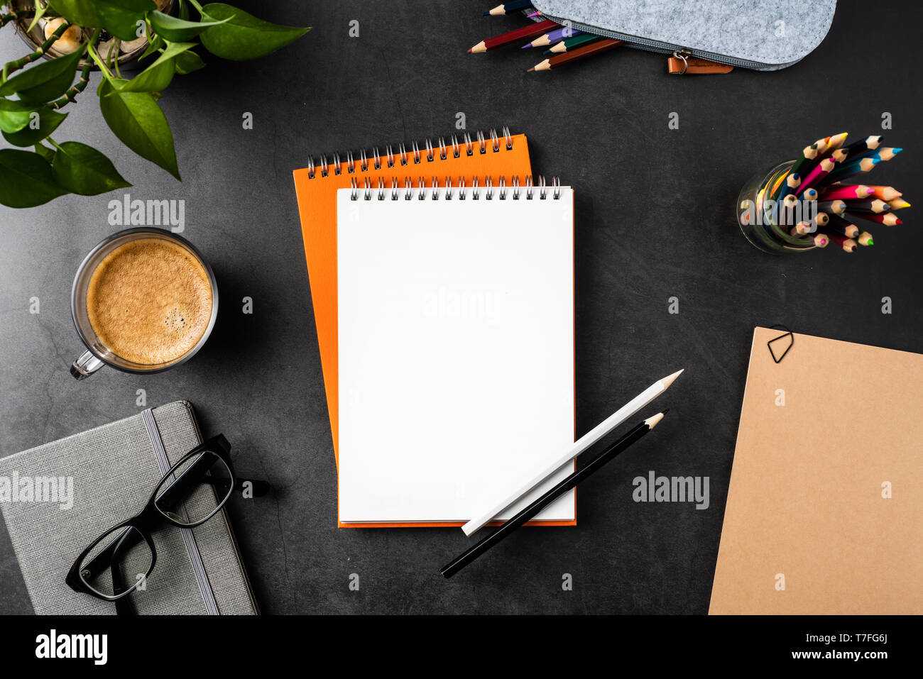 Designkonzept - Ansicht von oben kopieren Raum mit orangefarbenen Spirale notebook, Topfpflanze, Gläser, Kaffee, Bleistift auf schwarzen Hintergrund für mockup Stockfoto
