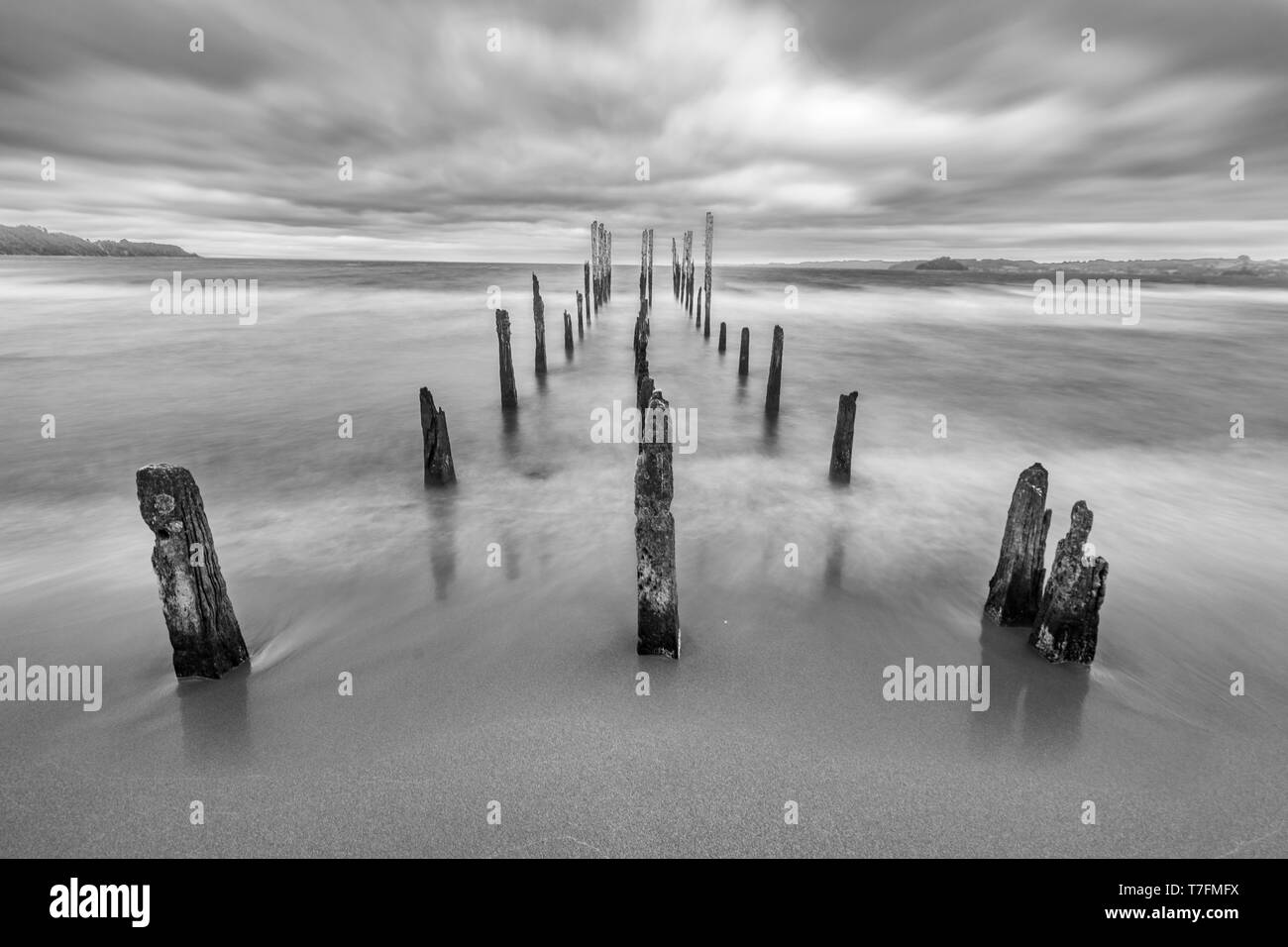 Wie eine Autobahn Hölle eine alte Pier im See Gewässer unter einem dramatischen bewölkten Himmel und starke Winde. Die alten hölzernen Pfosten noch kämpfen das Wetter Stockfoto