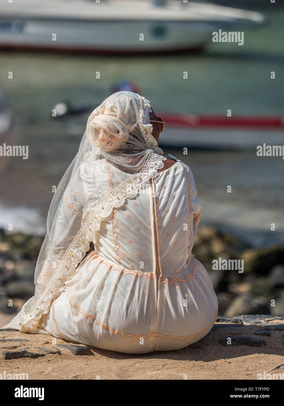 Blick auf senegalesische Frau in einem weißen Brautkleid sitzen am Meer auf der Insel Goree, Stockfoto
