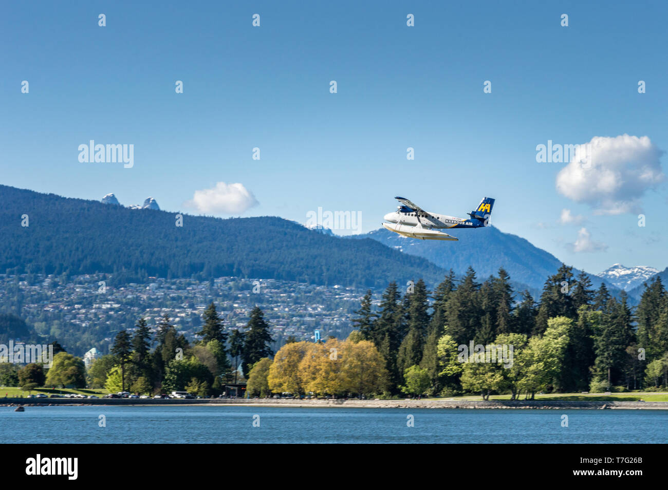 Vancouver, BC, - Mai 5, 2019: Harbour Air commuter plane flying Westen über Kohle Hafen. Stanley Park & North Shore Mountains im Hintergrund. Stockfoto