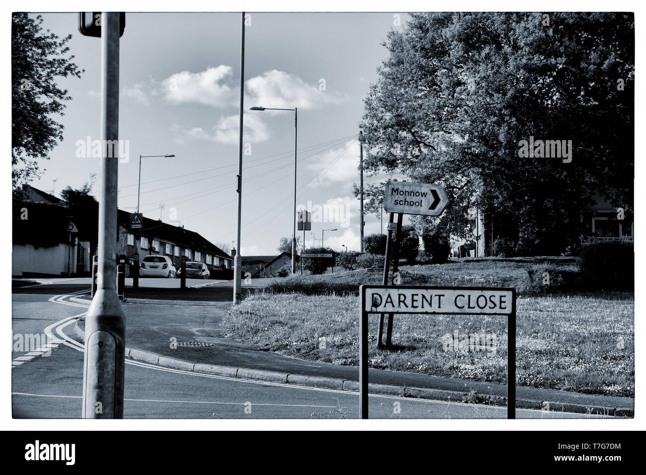 Schwarz-weißer Vorstadtstraßenszene an der Kreuzung Darent Close mit einem Richtungsschild für die Monnow School unter einem bewölkten Himmel, Newport, Wales Stockfoto