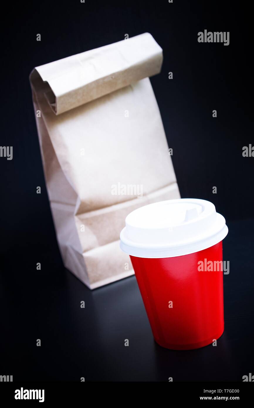 Rote Kaffeetasse und Papiertüte auf schwarzem Hintergrund. Coffee to go Stockfoto