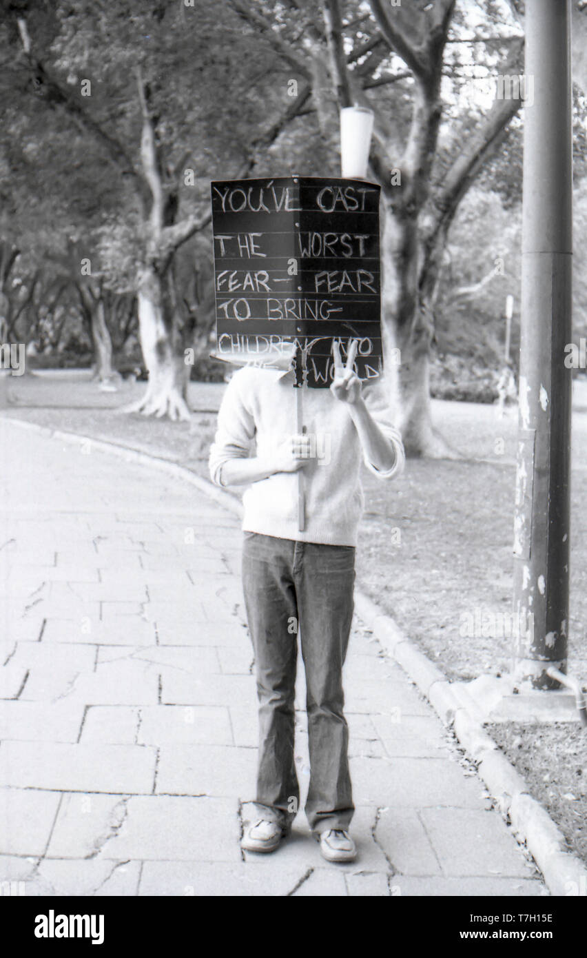 1977 Sydney, Australien: Eine anonyme Person hält ein Protest Plakat und macht ein Friedenszeichen in Sydney's Hyde Park nach einer anti-Uran März in der Stadt früh am Tag. Stockfoto