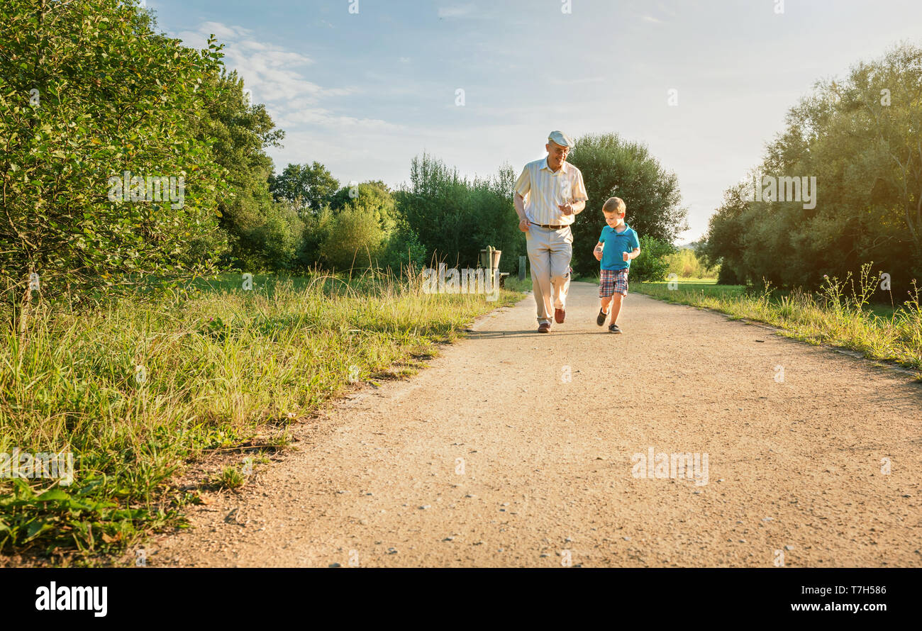 Vorderansicht des älteren Mannes mit Hut und fröhliches Kind läuft auf einem Pfad. Zwei verschiedenen Generationen Konzept. Stockfoto