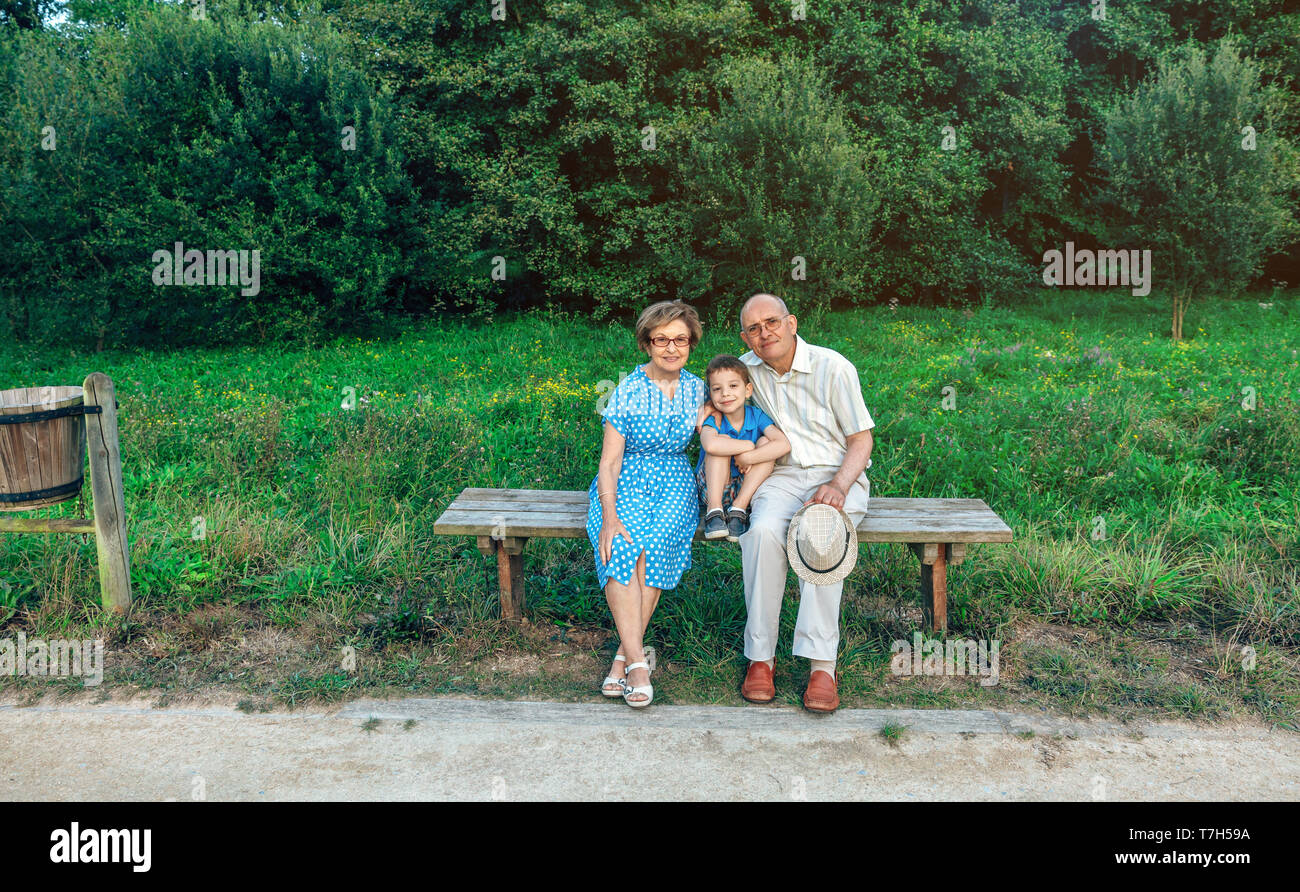 Großeltern und Enkel posieren für ein Foto sitzen auf einer Bank im Freien Stockfoto