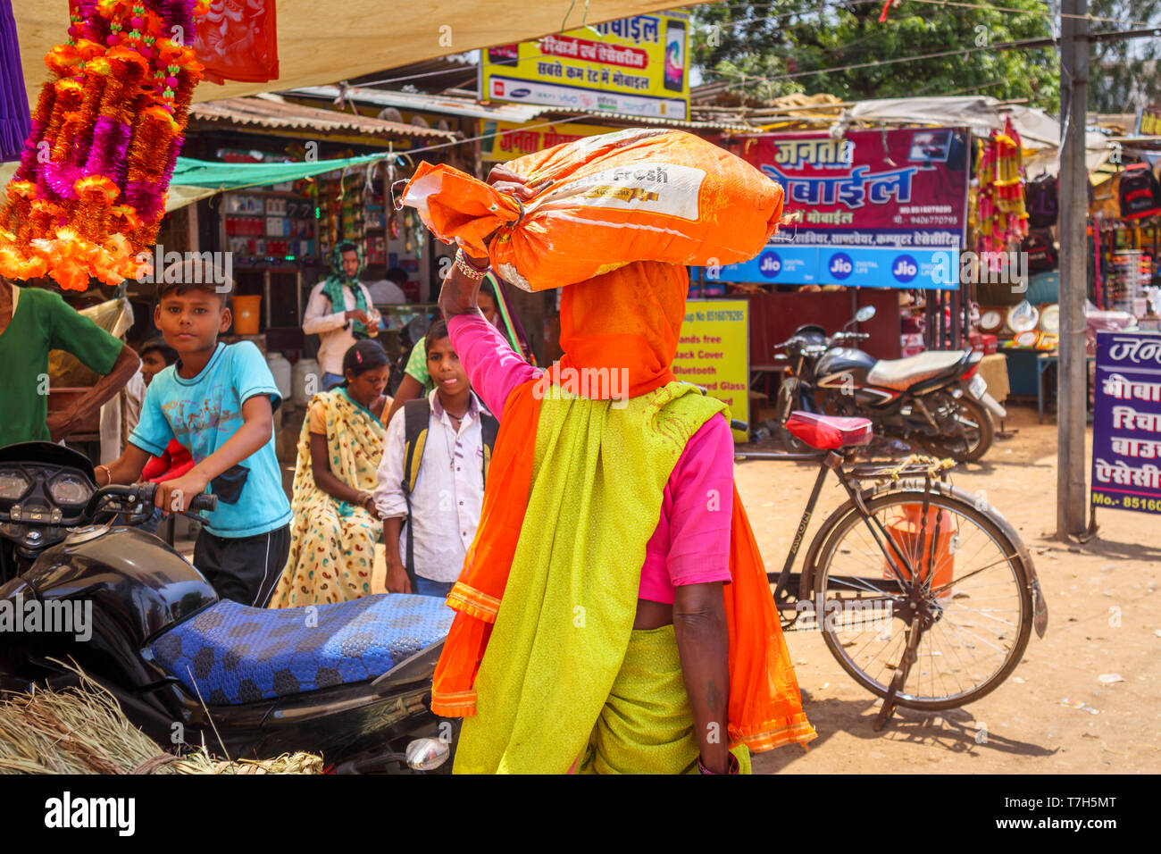 Straßenszene in Dindori Shahpura, eine Kreisstadt in der zentralen indischen Bundesstaat Madhya Pradesh, eine lokale Frau trägt ein Paket auf ihrem Kopf Stockfoto