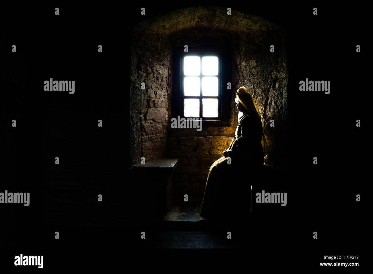 Teilweise Silhouette einer Frau in Mittelalterliches Kleid im Dunkeln zu sitzen, aus einem hellen Fenster in die Tiefen einer alten Burg Stockfoto