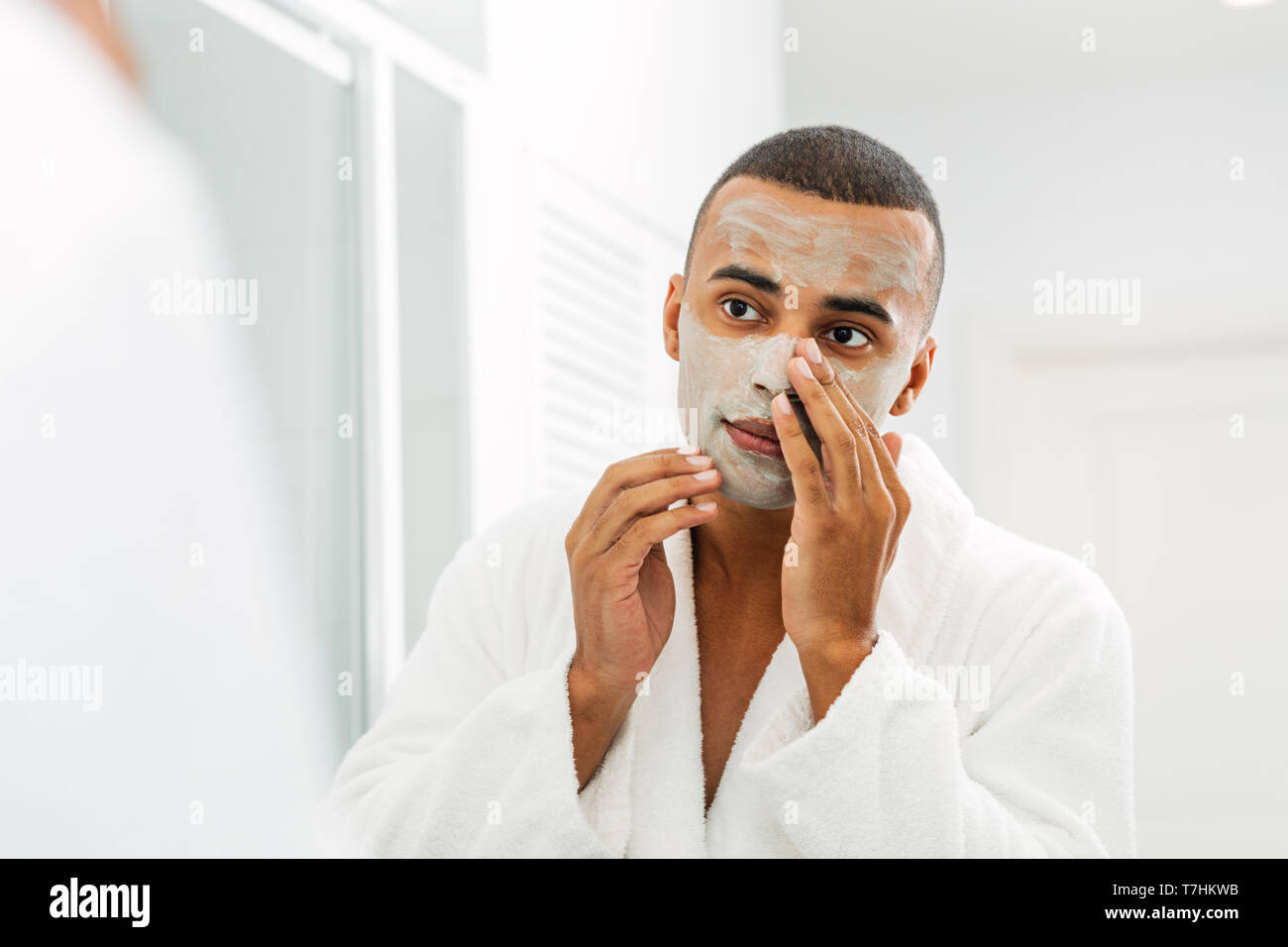 Junger Mann mit weißer Bademantel, die Gesichtsmaske im Badezimmer Stockfoto