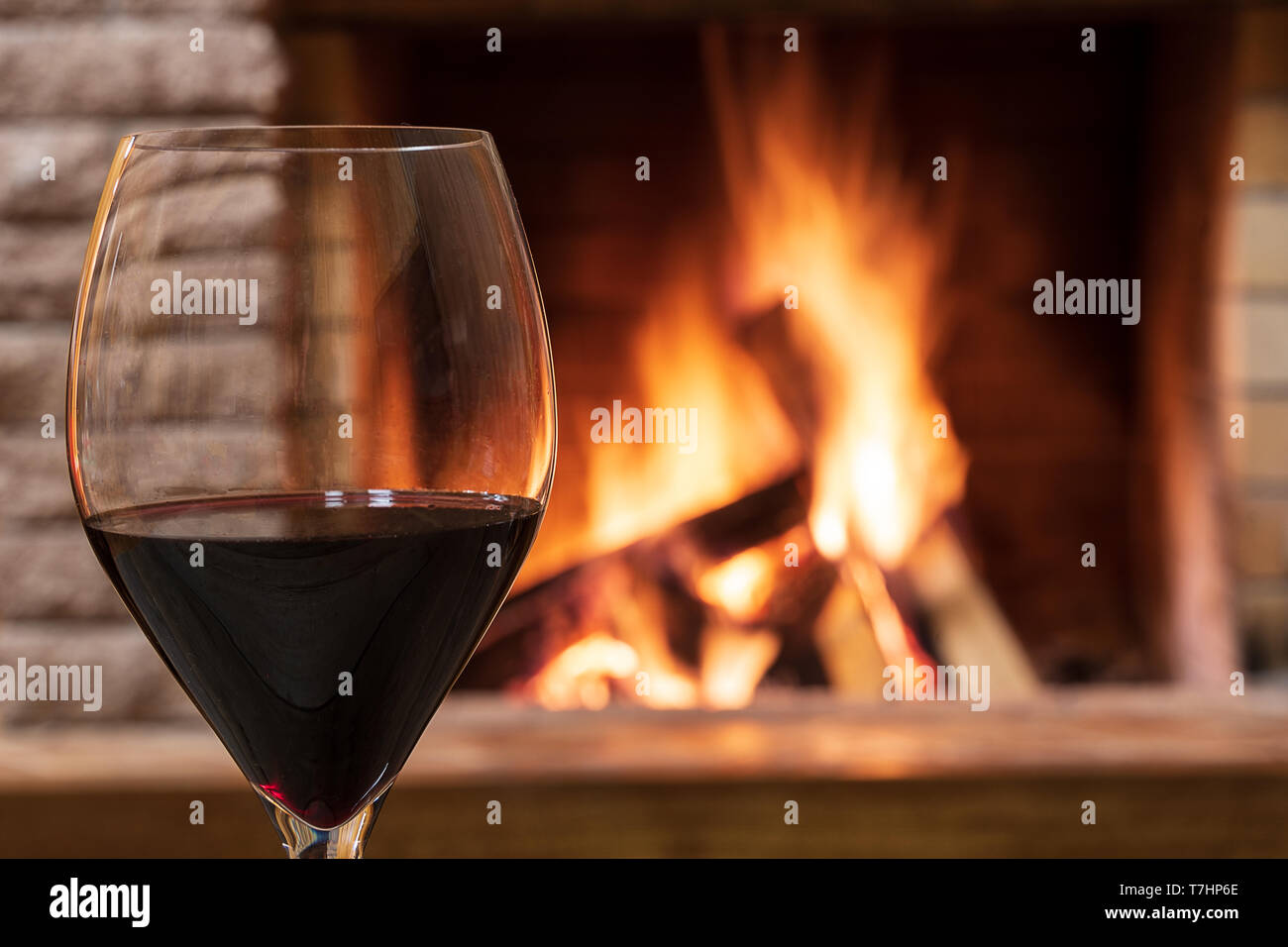 Glas Rotwein gegen gemütlichen Kamin Hintergrund, in Country House, horizontal, hygge, Home sweet home. Stockfoto