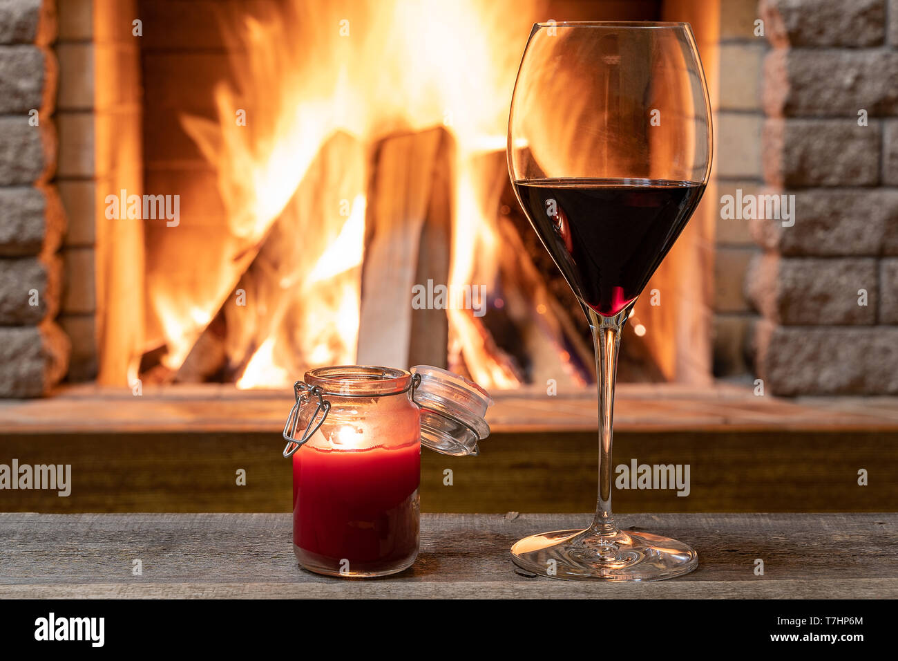 Glas Rotwein und Kerzenlicht gegen gemütlichen Kamin Hintergrund, in Country House, horizontal, hygge, Home sweet home. Stockfoto