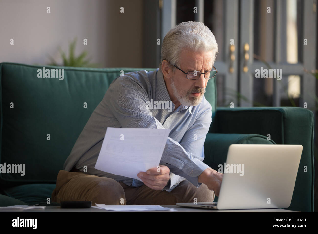 Grauhaariger reifer Mann Rechnungen berechnen, mit Laptop zu Hause Stockfoto