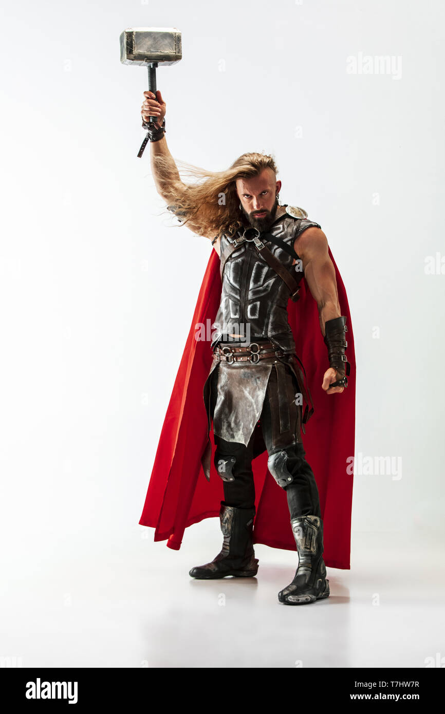Langes Haar und muskulös männliches Modell in der Viking leder Kostüm mit dem großen Hammer cosplaying Thor auf weißem studio Hintergrund isoliert. In voller Länge Porträt. Fantasy Warrior, antiken Schlacht Konzept. Stockfoto