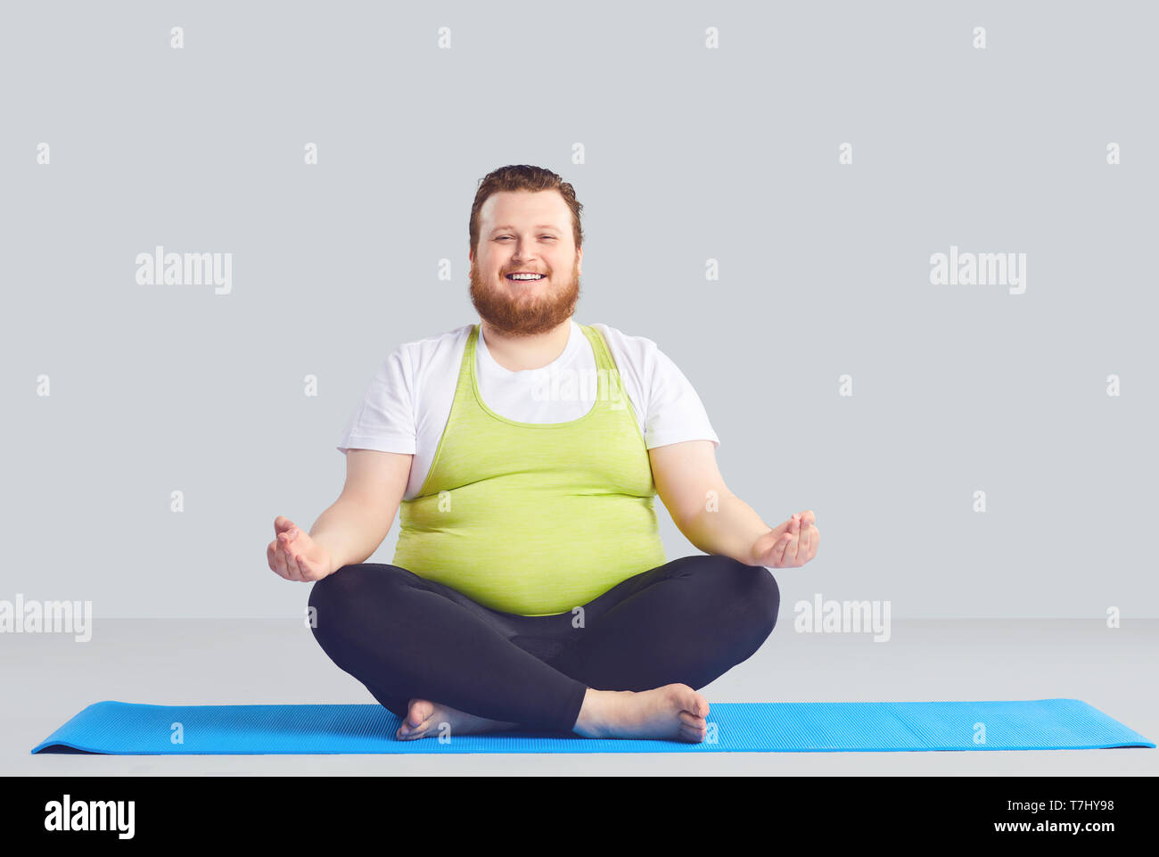 Positive fat man Yogi Yoga Übungen einen grauen Hintergrund. Stockfoto