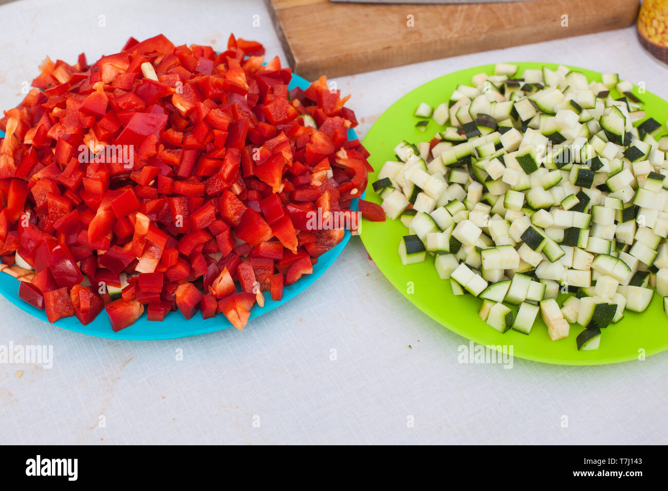 Eine blaue Platte voller gewürfelte rote roh Pfeffer und eine grüne Platte voller Grün raw gewürfelte Zucchini bereit, in die Pfanne zu erhalten Stockfoto