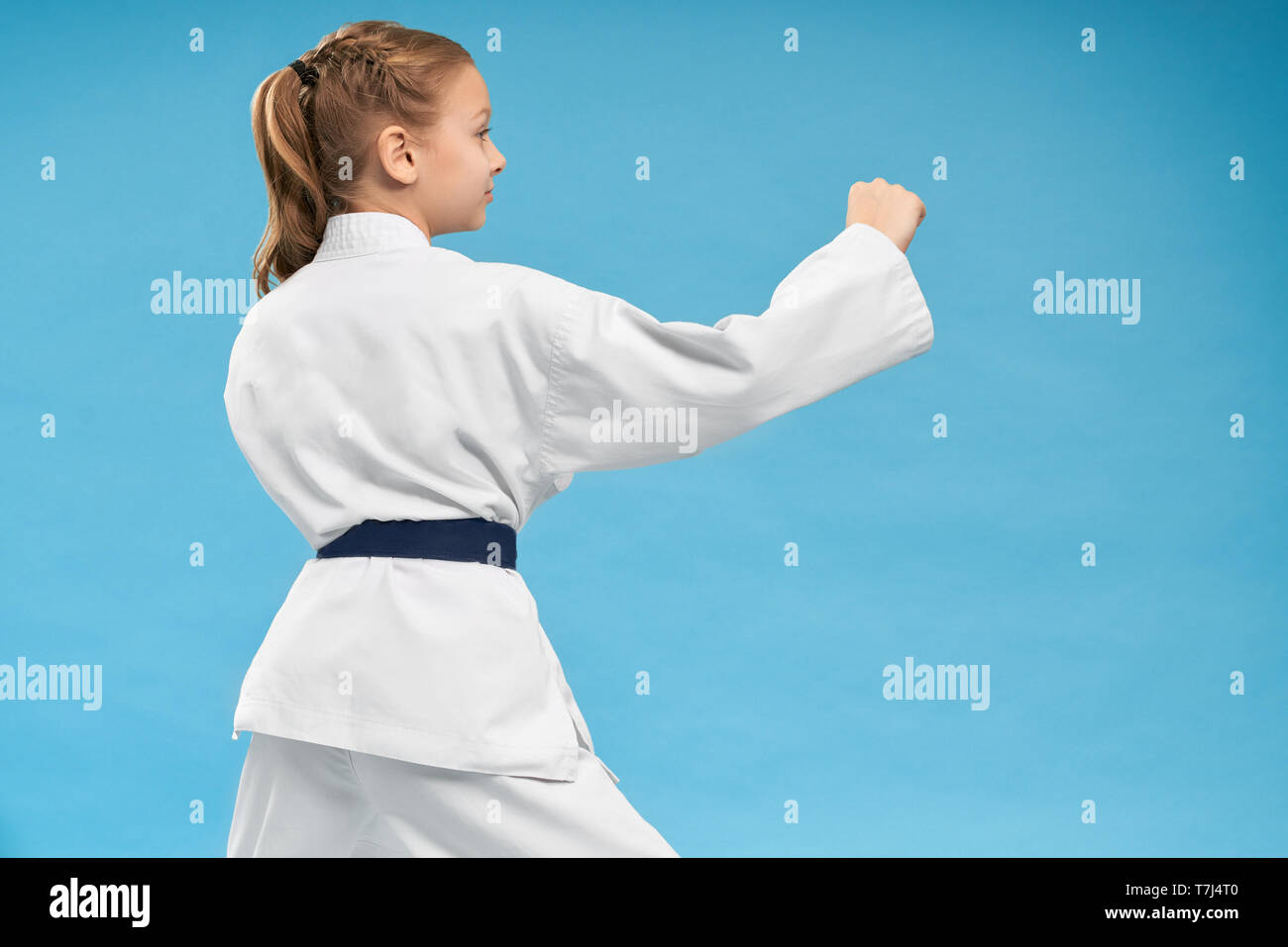 Ansicht von der Rückseite der aktiven Mädchen tun Karate auf blauem Hintergrund isoliert. Kleines Kind tragen Kimonos trainieren und Kämpfen im Studio. Hübsche Teenager tun Kampfsportarten Konzept der Sport. Stockfoto