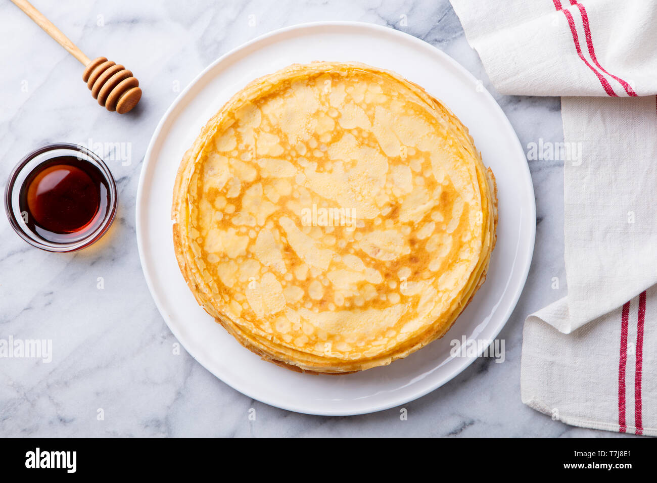 Crepes, dünne Pfannkuchen mit Honig auf eine weiße Platte. Marmor Hintergrund. Ansicht von oben. Stockfoto