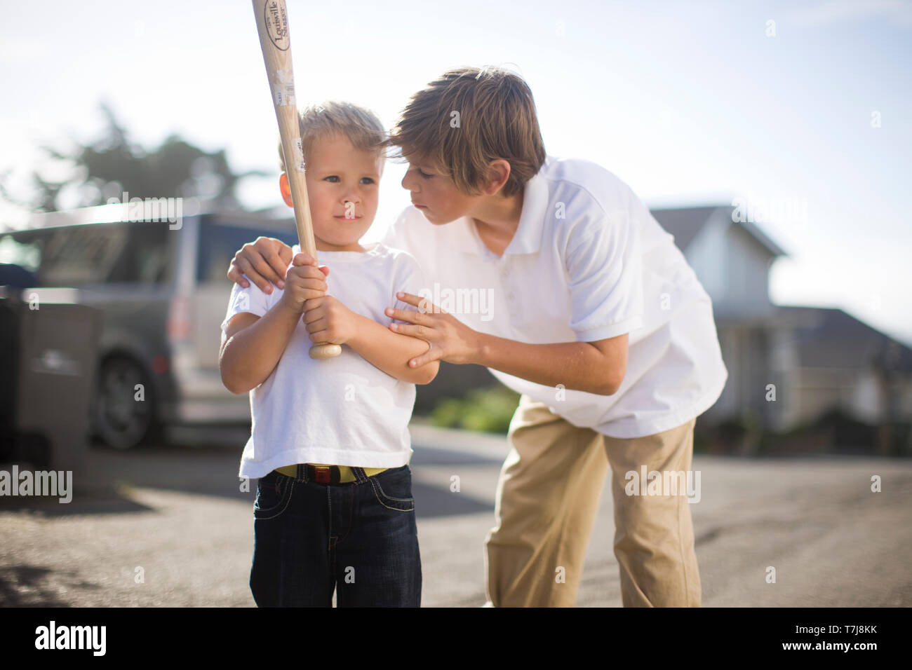 Junge sagt seinen jüngeren Bruder, wie seine Baseball Schläger zu schwingen auf der Straße. Stockfoto