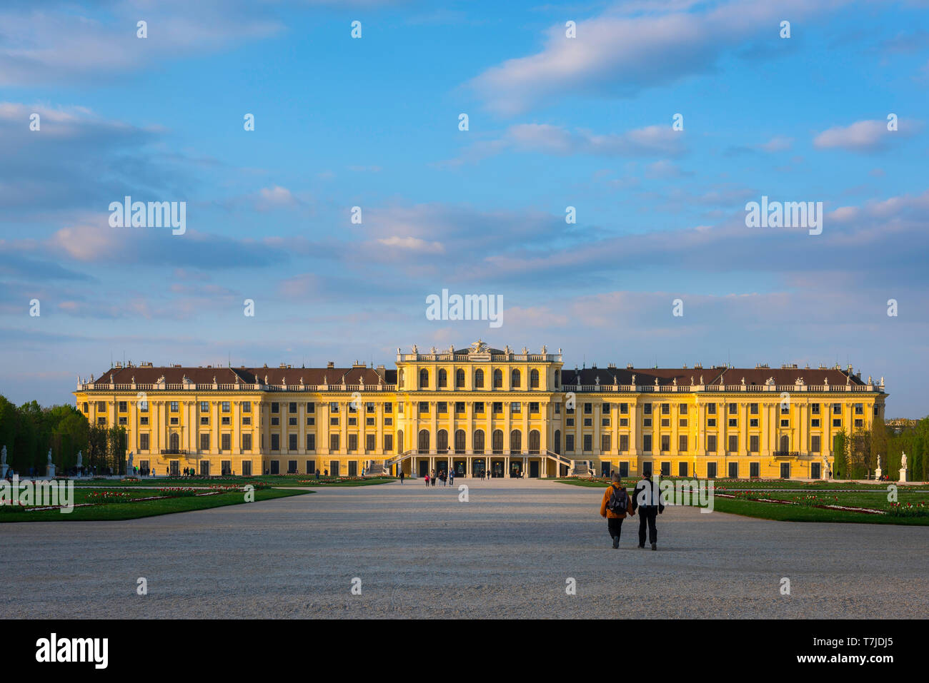 Schloss Wien, Blick bei Sonnenuntergang auf ein Ehepaar mittleren Alters, das auf die Südseite des historischen Schlosses Schönbrunn in Wien, Österreich, geht. Stockfoto