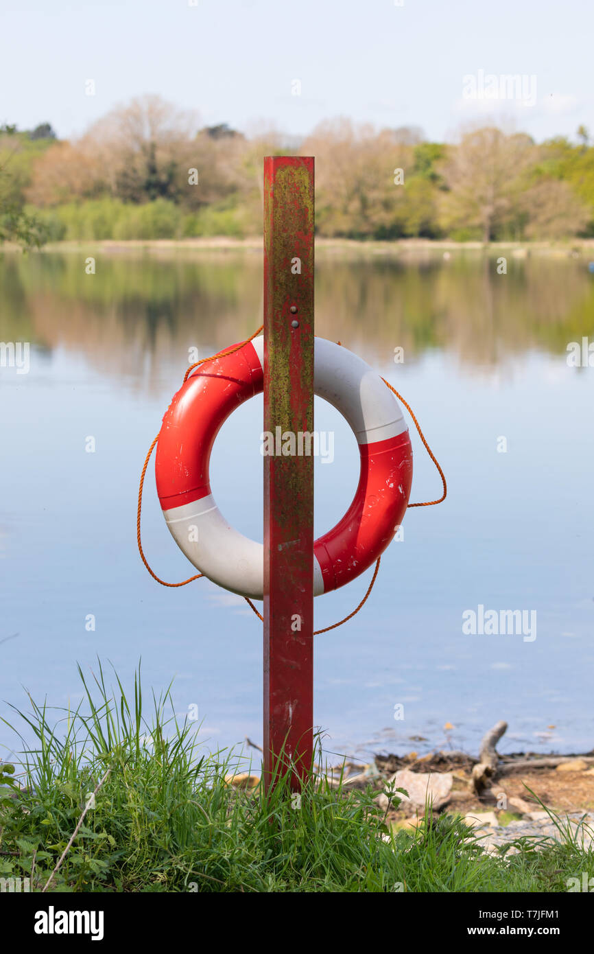 Eine rot-weiße Life Saver Ring hängt ein roter Pfosten am Ufer eines Behälters. Orange Seil hängt lose um den Ring. Stockfoto