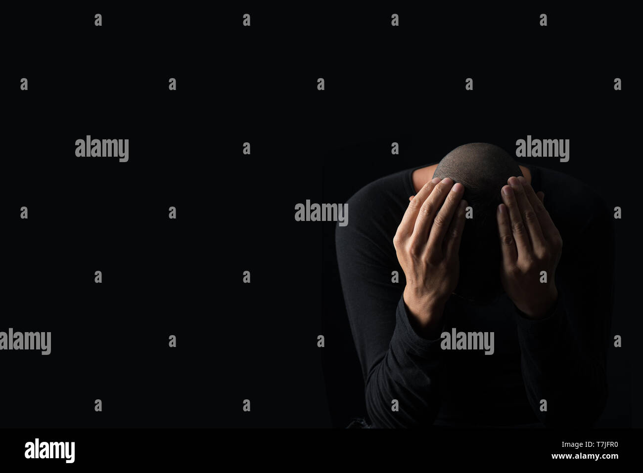 Nahaufnahme eines verzweifelten jungen kaukasischen Mann mit seinen Händen in seinen Kopf, auf einem schwarzen Hintergrund, mit einigen leeren Raum auf der linken Seite Stockfoto