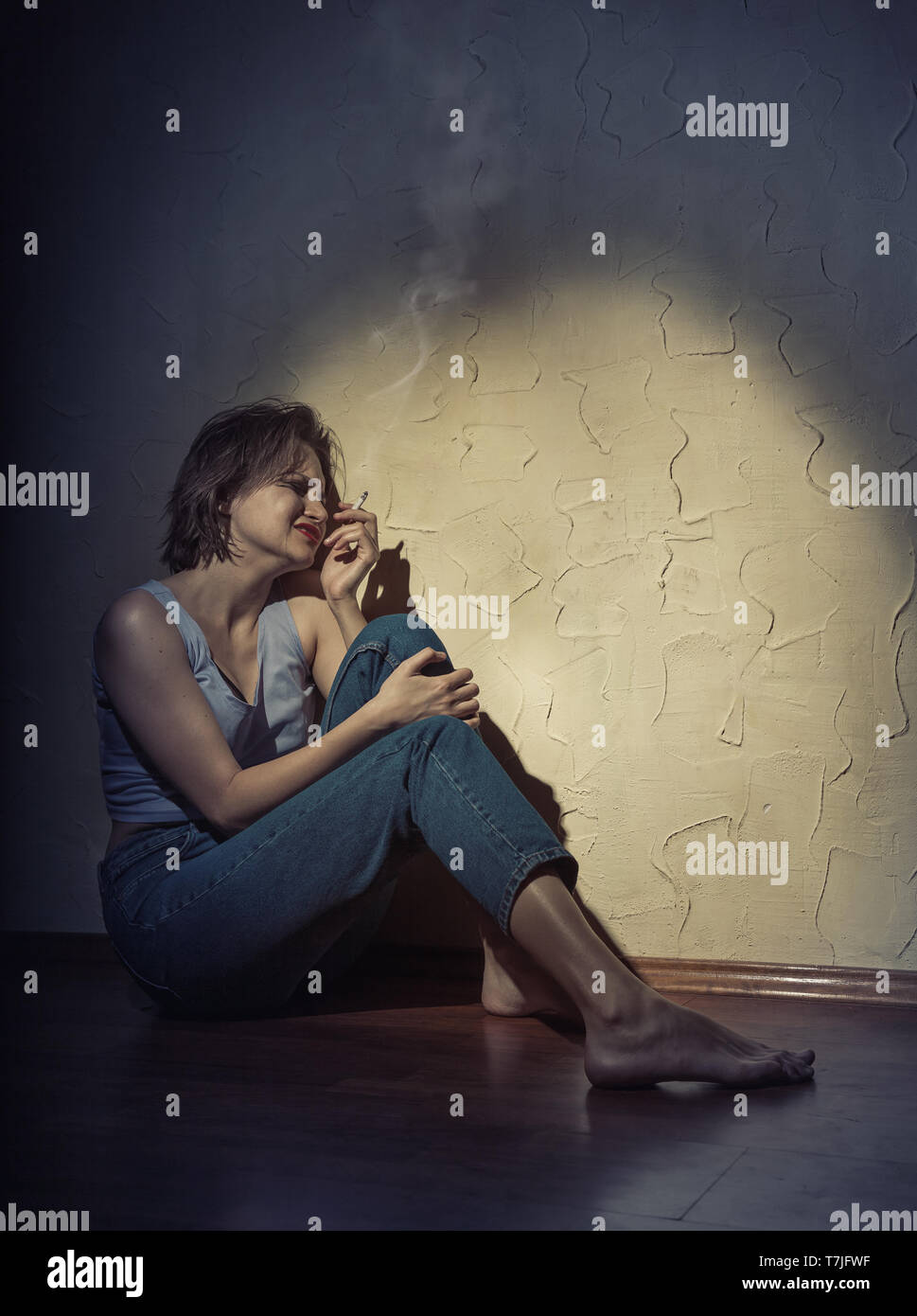 Eine junge Frau mit einer Zigarette in der Hand auf dem Boden sitzend Stockfoto