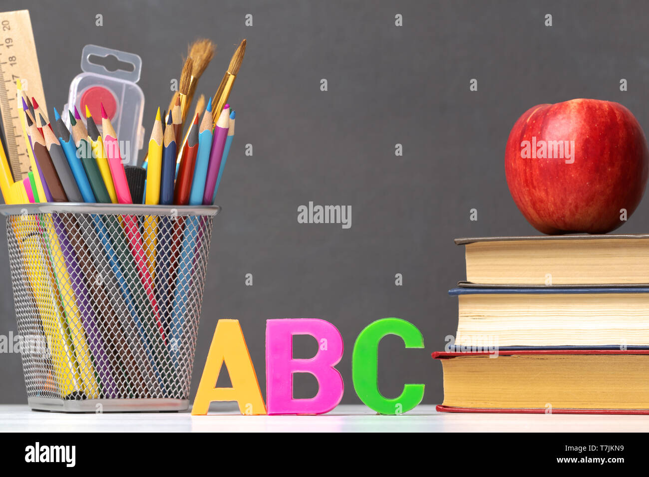 Eine Reihe von Schulmaterial. Ein Stapel von Lehrbüchern, ein Apfel, Buchstaben A, B, C, Stifte, Pinsel, Farben, gegen eine Schwarze Schiefertafel. Die co Stockfoto