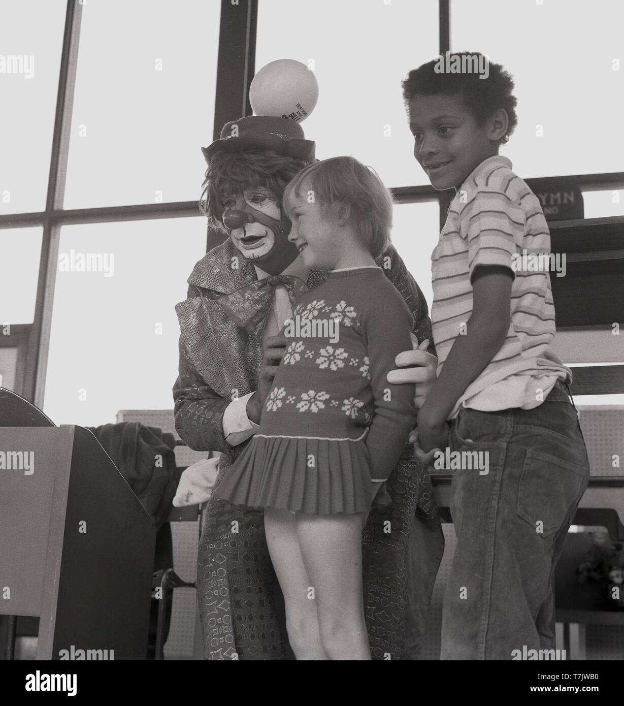 1960, historische, einem Zirkus Clown Besuch einer Grundschule, auf der Bühne mit zwei jungen Schüler, South London, England, UK. Stockfoto