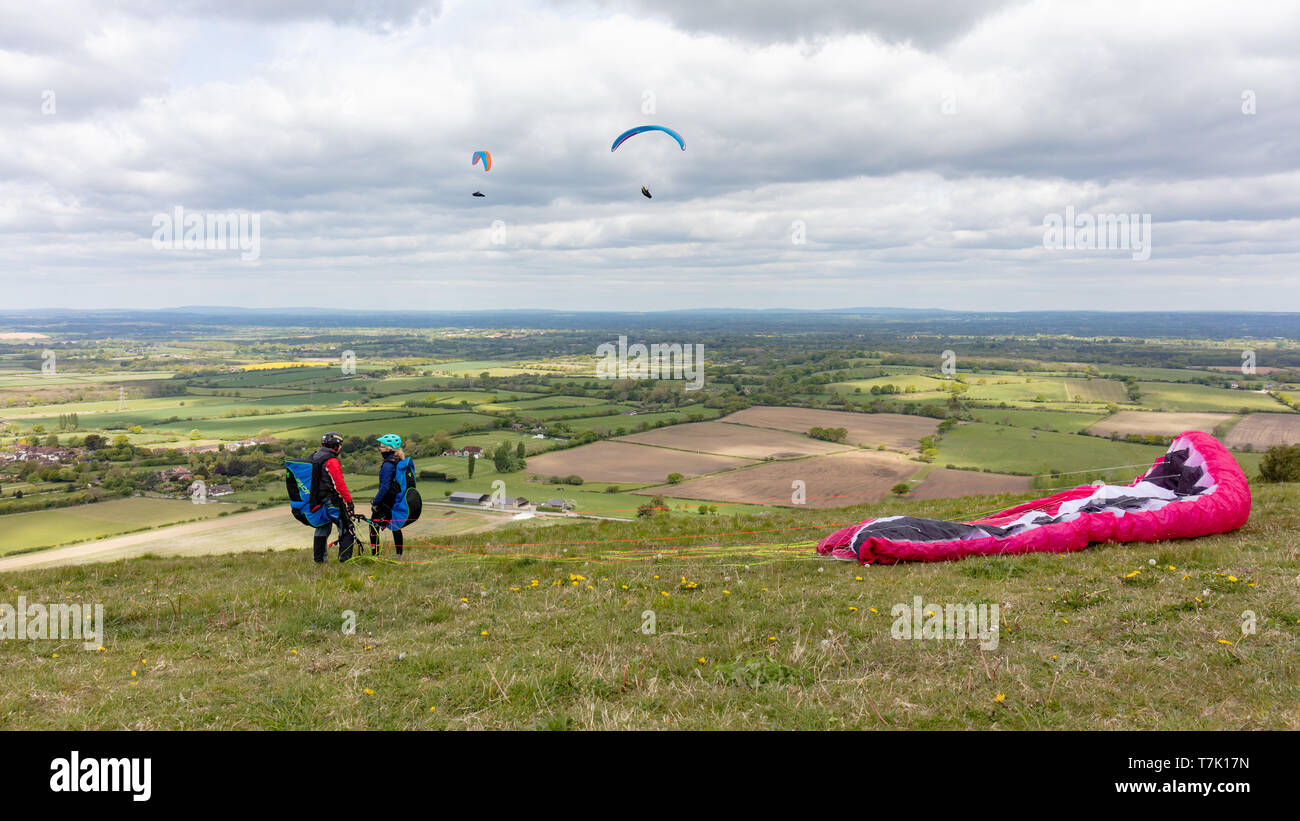 Devils Dyke, Sussex, UK; 6. Mai 2019; Männlich und Weiblich Gleitschirme mit der Haube auf dem Boden. Zwei Gleitschirme hinter Ihnen fliegen Stockfoto
