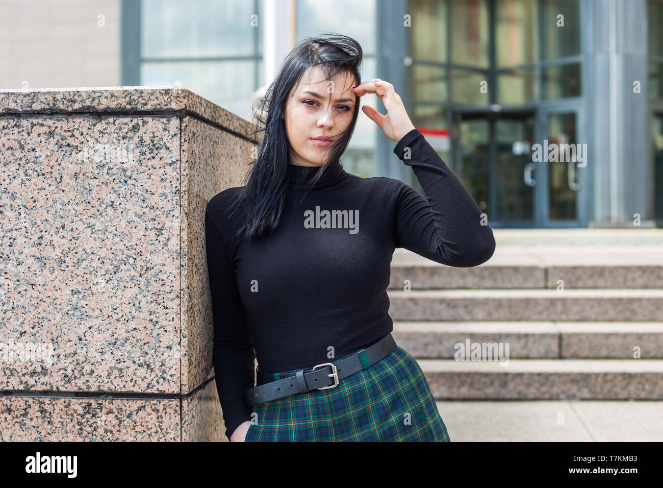 Junge Frau in schwarzen T-Shirt und schwarze Haare stehen vor dem Bürogebäude, halb Körper, Vertrauen Stockfoto