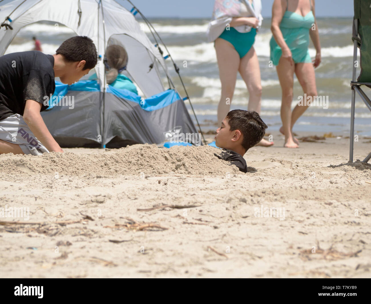 Ein Junge ist in Sand an einem sonnigen Tag am Strand in Port Aransas, Texas USA begraben. Stockfoto