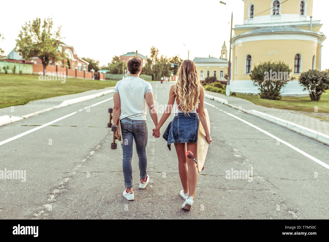 Ein junges Paar Wanderungen im Sommer in der Stadt, in den Händen von skateboards, longboard. Ansicht von hinten. Spaziergang am Wochenende, Lebensstil der jungen Menschen. Stockfoto