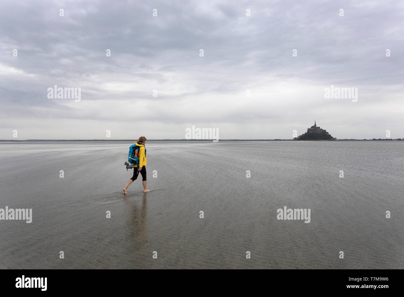 Frau in gelber Jacke, Wandern mit einem Rucksack barfuß auf Sand bei Ebbe  durch die Bucht von Mont Saint Michel, Normandie, Frankreich  Stockfotografie - Alamy