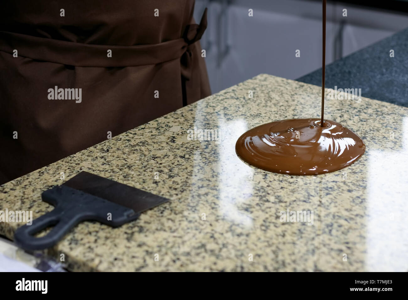 Chocolatier in eine braune Schürze gießt flüssige Schokolade auf einem Granit Tisch Stockfoto